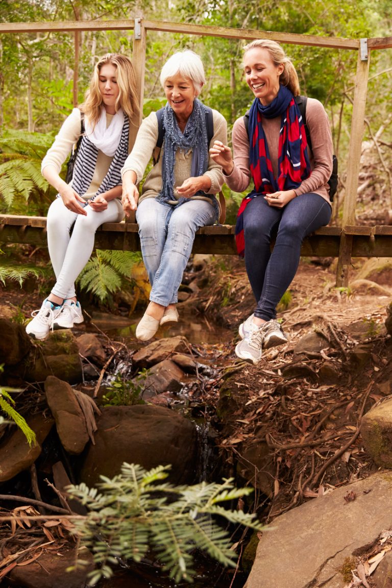 Three generations of women sitting on a bridge in forest